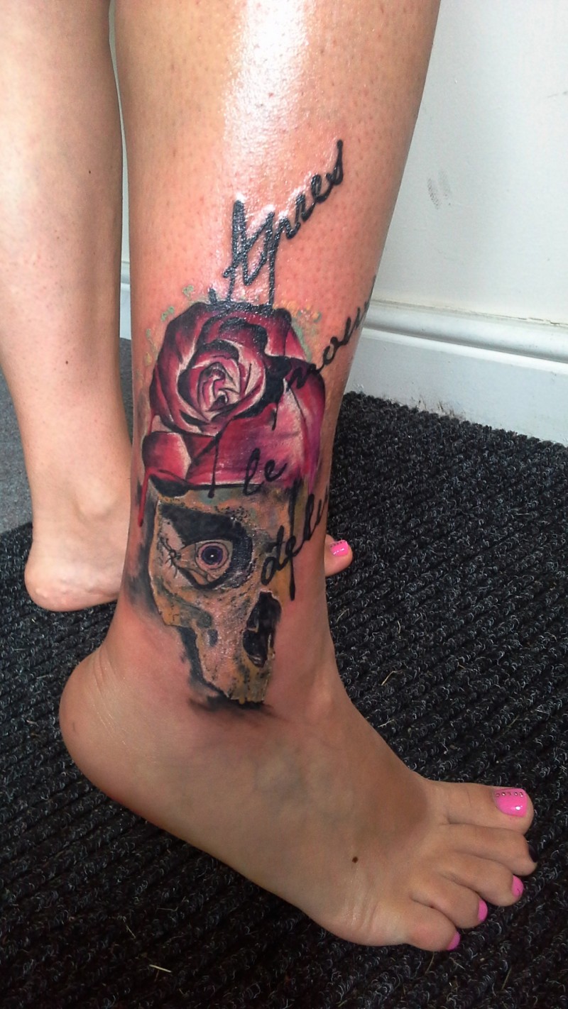Modern traditional style colored ankle tattoo of human skull with rose and lettering