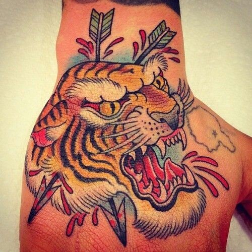 Multicolored old school style furious tiger&quots head with arrows bloody tattoo on hand