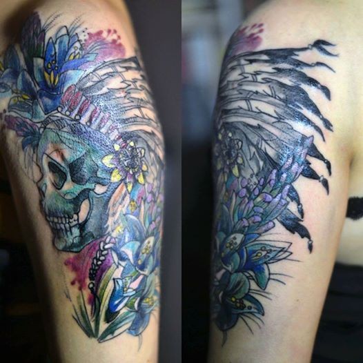 Multicolored upper arm tattoo of Indian skull with helmet and flowers by Joanna Swirska