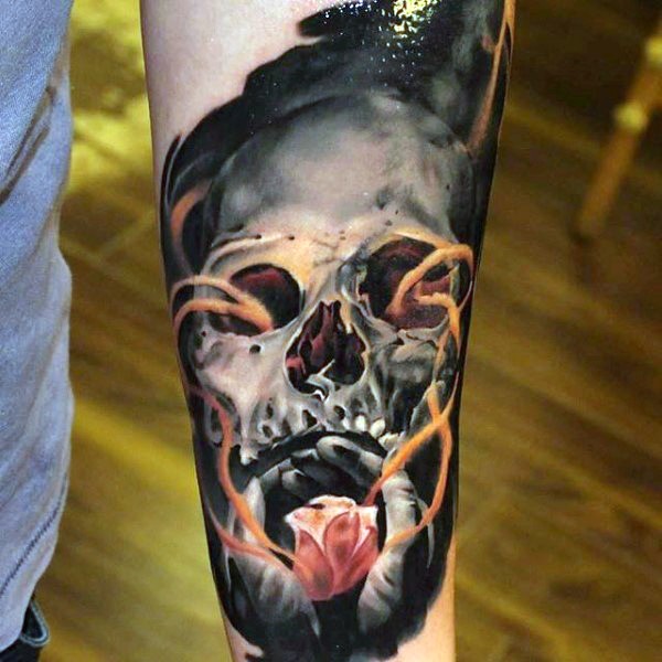 Tatuaje en el antebrazo, cráneo humano misterioso y manos con flor