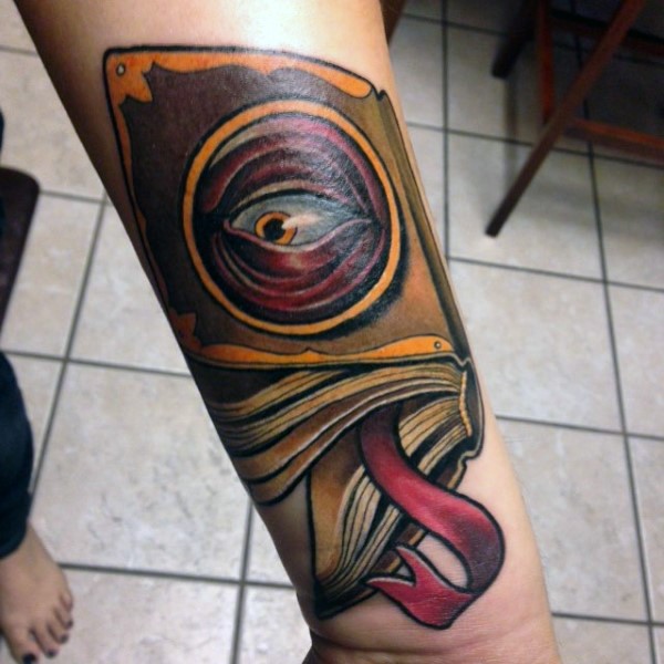 Mystical illustrative style colored forearm tattoo of spell book with eye