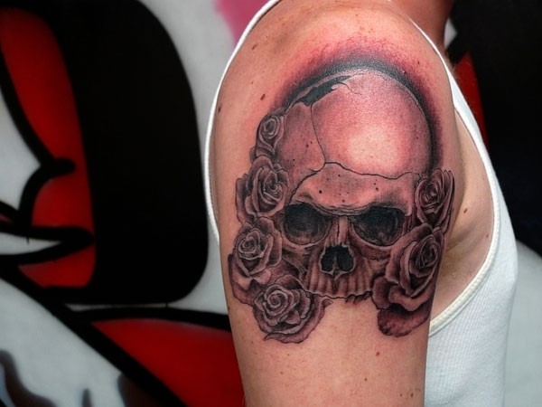 Natural looking accurate painted black ink broken skull tattoo on shoulder with rose flowers