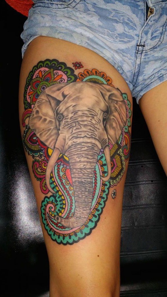 Natural looking colored elephant tattoo on thigh combined with Hinduism themed ornaments