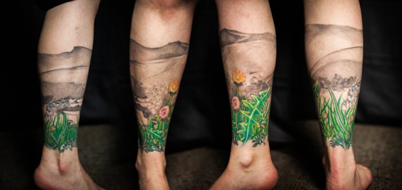 Natural looking colored leg tattoo of flowers and mountains