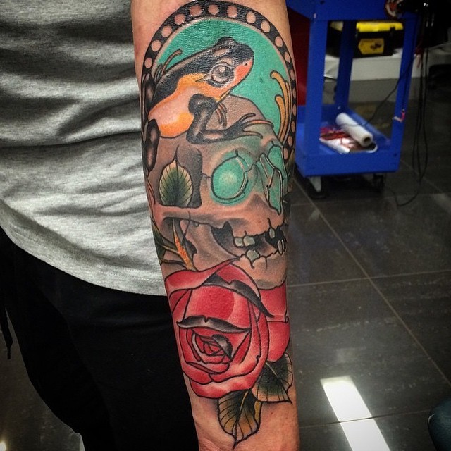 Neo traditional style colored arm tattoo of human skull with frog and rose