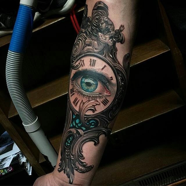 New school style colored vintage clock forearm tattoo stylized with blue eye