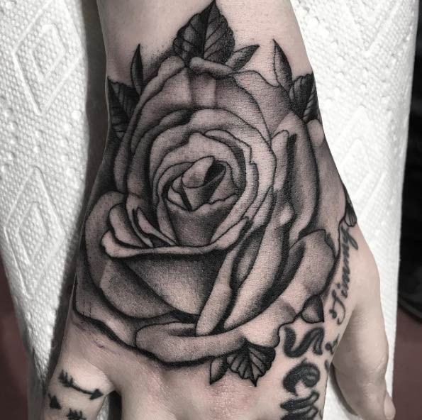 Schönes detailliertes schwarzes Rose Tattoo an der Hand mit Blättern