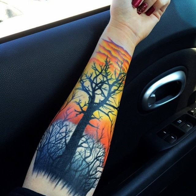 Nettes mehrfarbiges Unterarm Tattoo mit dunklem Baum und Sonnenuntergang
