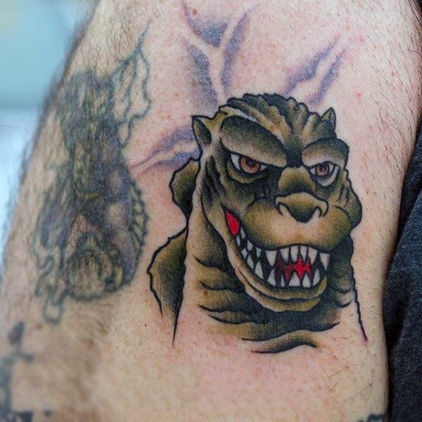 Old cartoon style painted little Godzilla face tattoo on arm