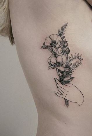 Old looking detailed side tattoo of hand holding flowers by Zihwa