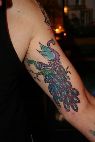 Tatuaje en el brazo en colores brillantes dos pavos reales