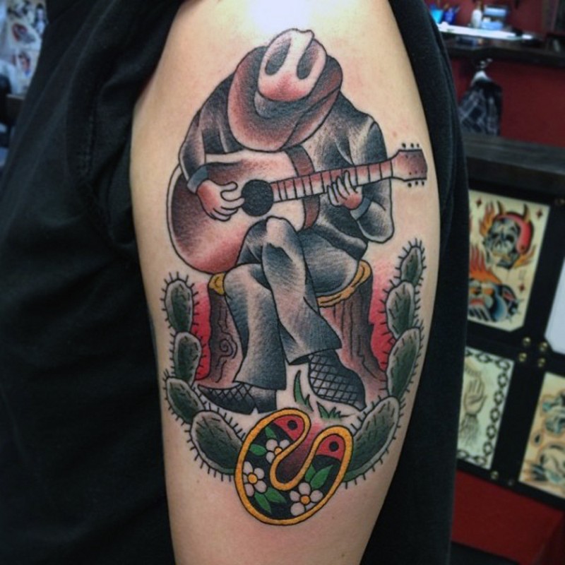 Tatuaje en el brazo,
vaquero que toca la guitarra entre cactos, old school