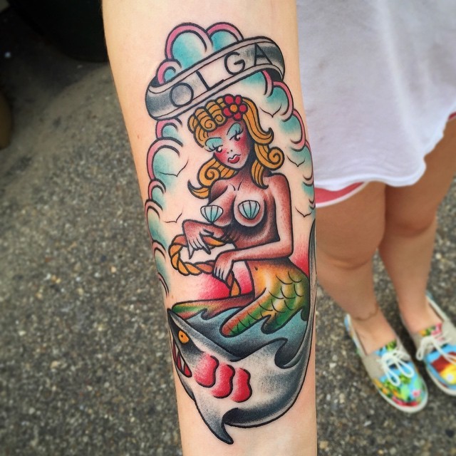 Old school colored mermaid and shark tattoo on forearm stylized with lettering