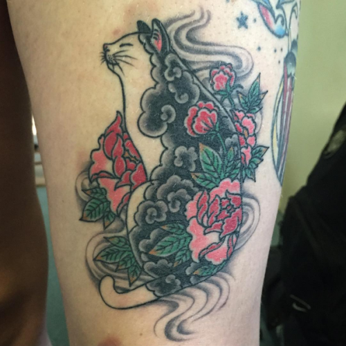 Old school colored thigh tattoo of funny cat stylized with red flowers