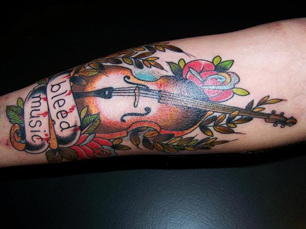 Old school colored violin tattoo on forearm with flowers and lettering