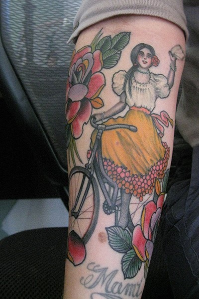Old school multicolored forearm tattoo of woman on bicycle with flowers