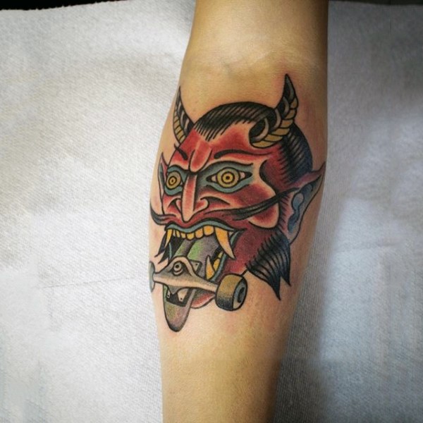 Old school small colored devil with skateboard tattoo on forearm