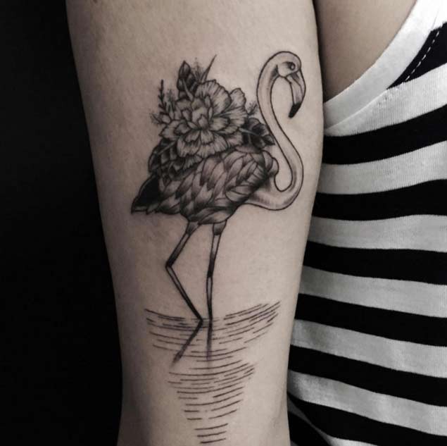 Old school style black and white flamingo tattoo on arm stylized with flower