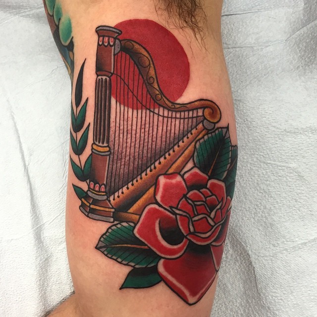 Old school style colored biceps tattoo of harp with flower