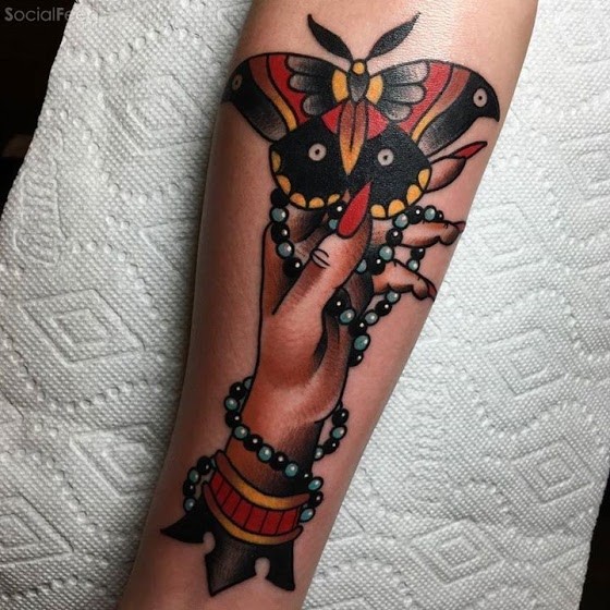 Old school style colored forearm tattoo of woman hand with butterfly and jewelry