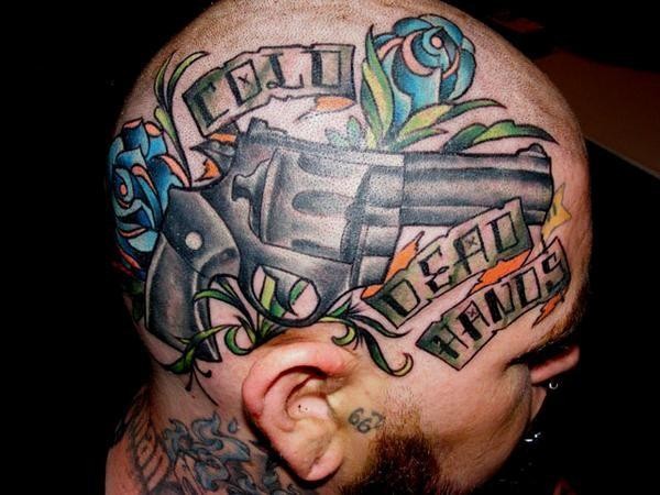 Old school style colored head tattoo of big pistol with flowers and lettering