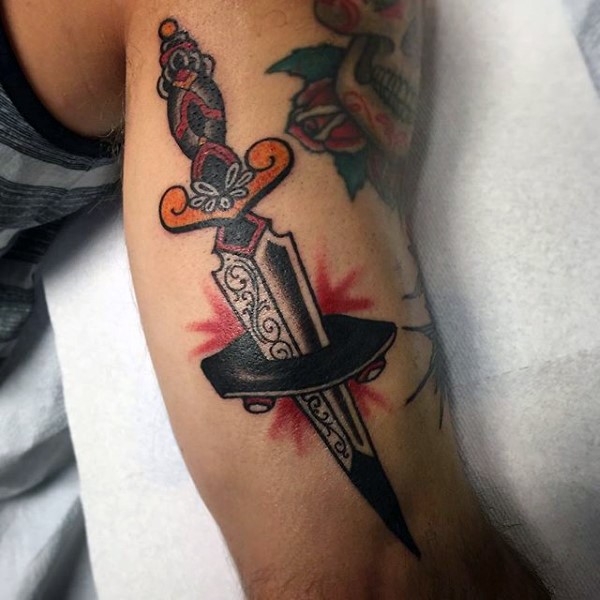 Old school style colored sharp dagger into skateboard tattoo on biceps