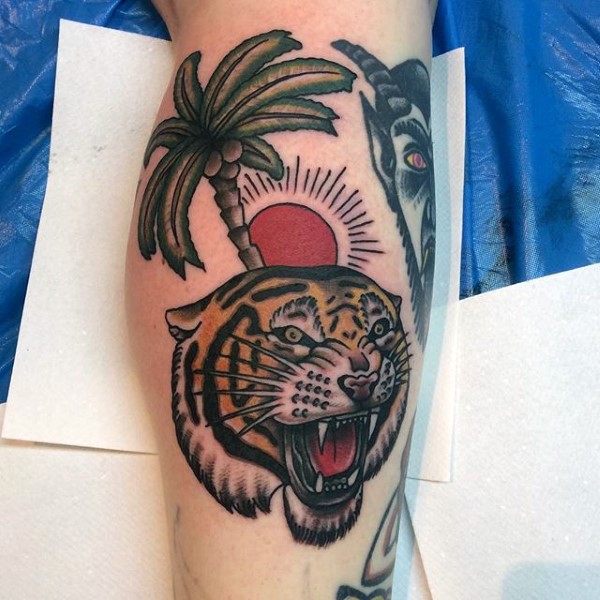 Old school style designed colored roaring tiger with palm tree tattoo on leg