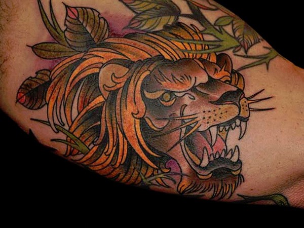 Old school style multicolored lion tattoo on arm with leaves