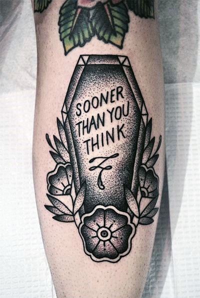 Tatuaje en el brazo, ataúd con escrito y flores, colores negro y blanco