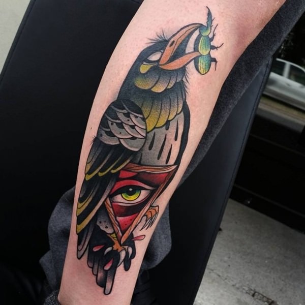 Tatuaje en el antebrazo, cuervo extraordinario con escarabajo en el pico y ojo misterioso en el vientre