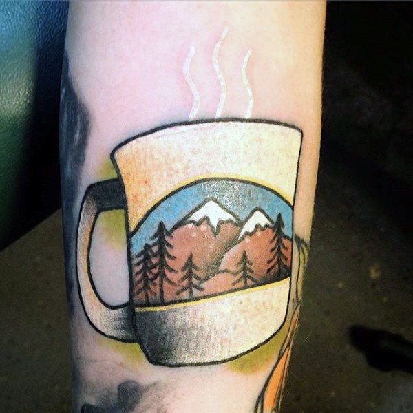 Tatuaje en el antebrazo, taza con bebida caliente y  con dibujo de paisaje con montaña