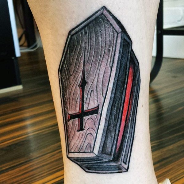 Tatuaje en el tobillo,  ataúd de madera con cruz grabada en la tapa