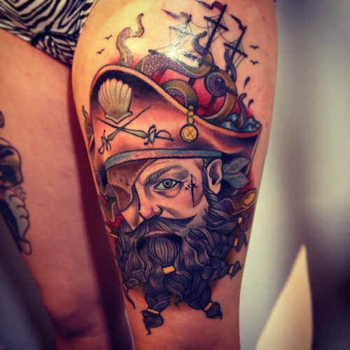 Old style painted colored pirate with ship tattoo on thigh