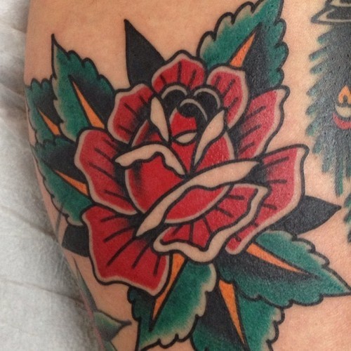 Old style painted simple colored little rose tattoo on leg