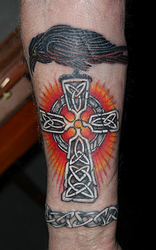 Original colored Celtic style cross tattoo on forearm with crow