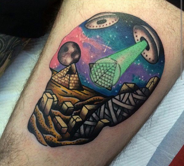 Original designed skull shaped colored tattoo on thigh stylized with alien ships building Egypt pyramids