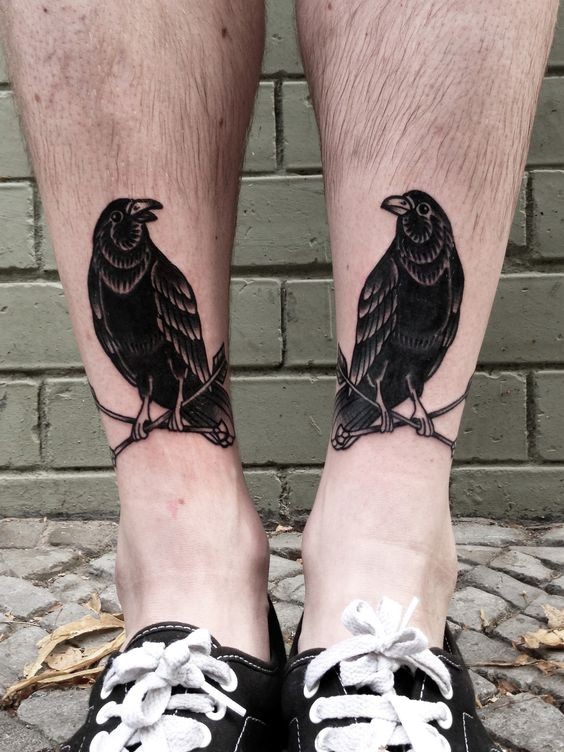Ein Paar von schwarzen Krähen sitzt auf gekreuzten Pfeile Tattoo an beiden Beinen