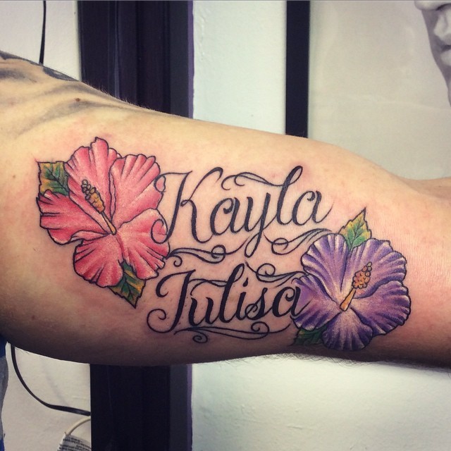 Pink and violet hibiscus flowers and lettering memorial tattoo on biceps