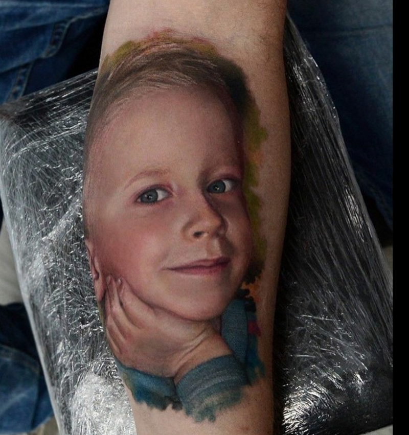 Portrait style colored forearm tattoo of cute looking smiling boy