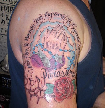 Tatuaje en el hombro las manos rezando con una inscripción