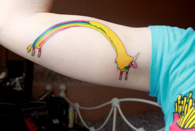 Rainbow shaped and colored funny unicorn tattoo on teenage biceps