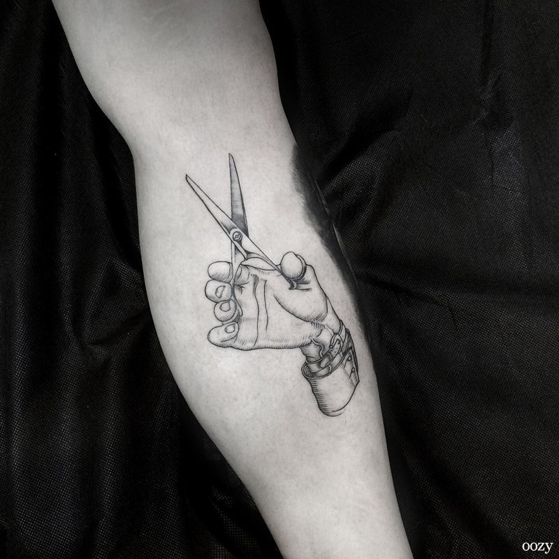 Tatuaje en el antebrazo,
dibujo simple de mano con tijeras, tinta negra