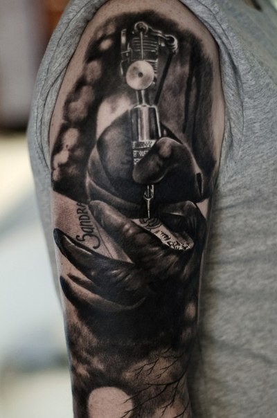 Realism style black ink shoulder tattoo of hand with tattoo machine