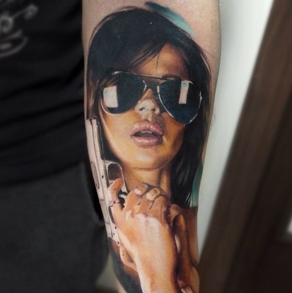 Realism style colored forearm tattoo of sexy woman with pistol and sun glasses