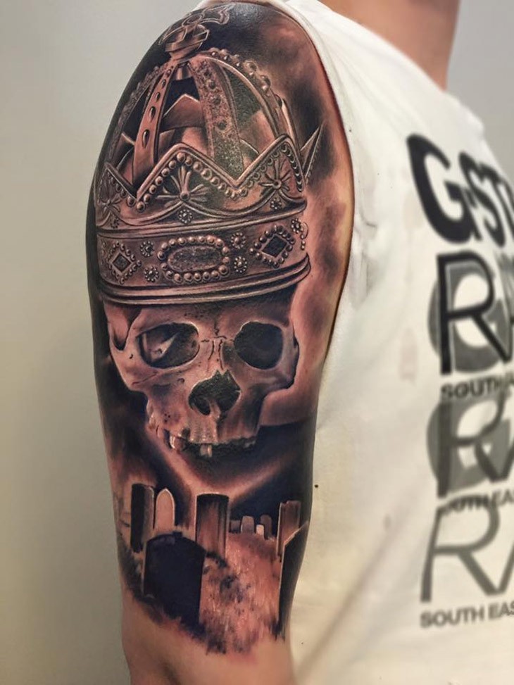 Realism style colored shoulder tattoo of human skull part with big beautiful crown and cemetery