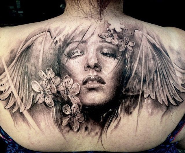 Realism style colored upper back tattoo fo woman face with wings and flowers