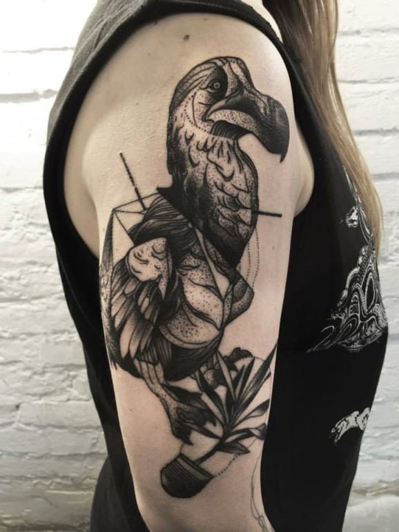 Realistic looking blackwork style upper arm tattoo of large bird with leaves by Michele Zingales