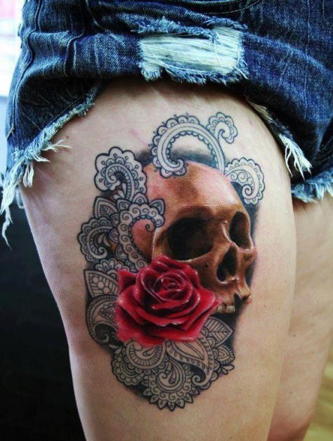 Realistic skull with red rose and black patterns tattoo on thigh for women by Kata Urban