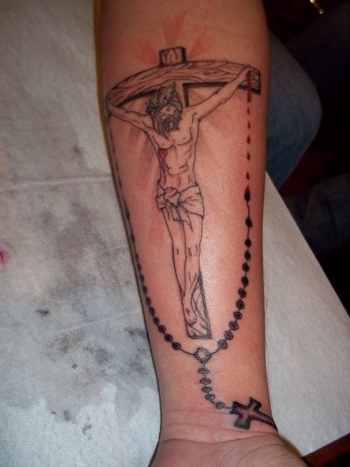 Religious gray-ink Jesus on cross with beads tattoo on forearm