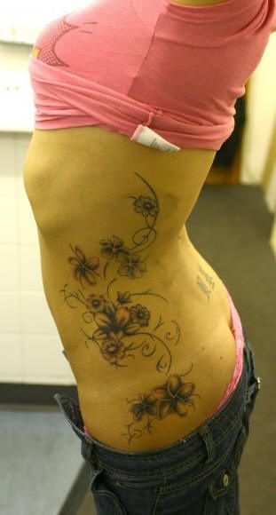 Le tatouage sur le flanc avec une plante décorée de fleurs différentes